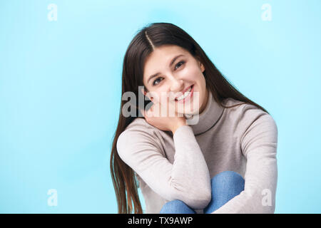 studio portrait of a beautful caucasian woman, sitting on floor, looking at camera smiling, isolated on blue background Stock Photo