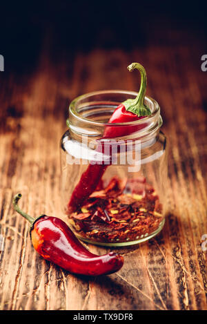 Two dried red chili peppers in jar with ground peppers Stock Photo