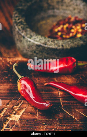 Sun dried red chili peppers on wooden surface with mortar and pestle Stock Photo