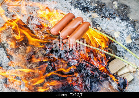 Grilling sausages over an open fire outdoors Stock Photo