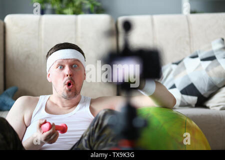 Male vlogger holds dumbbells in his hands and shouts at the camera on his subscriber, motivating them to action. Tutoring grade on an individual progr Stock Photo