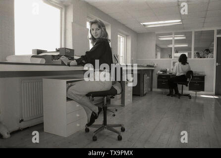 1980s, a young female in a bright design office with a wooden floor sitting on a swivel chair by a large window, working on a type of electronic data processor with a keyboard and sitting on top of it, a GSi scanner or laser printer, England, UK. Stock Photo