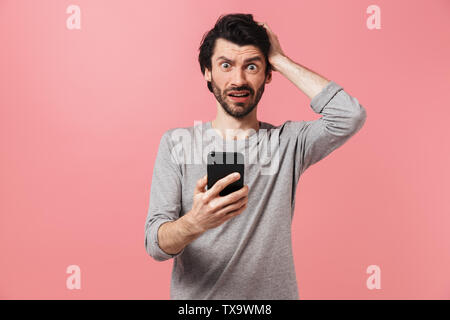 Image of a handsome confused serious young man isolated over pink wall background using mobile phone. Stock Photo