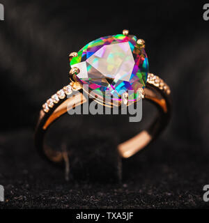 Gold ring, decorated with a large stone, iridescent in different colors on a dark background Stock Photo