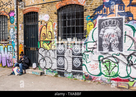 Woman sitting in front of graffiti in the famous Shoreditch Graffiti Wall at Seven Stars Yard, a yard filled with street art near Brick Lane