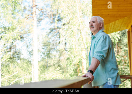 Senior grey-haired man in blue shirt standing on terrace Stock Photo