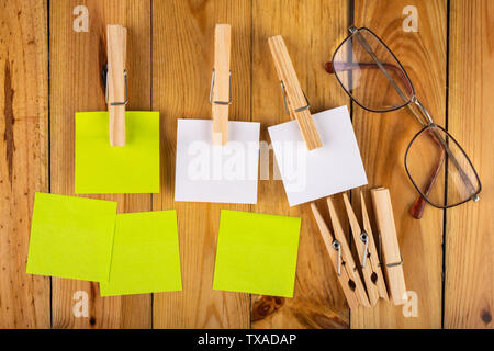 Colorful sticky notes hung on wooden clips. Sticky notes for saving reminders on a wooden table. Light background. Stock Photo