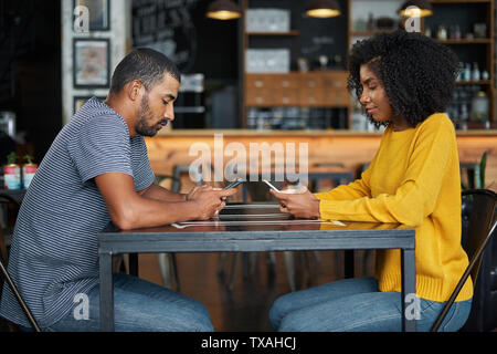 Couple at café table using mobile phones Stock Photo