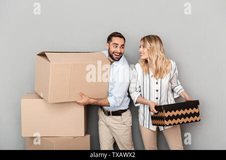 Photo of nice european couple in casual clothing looking at each other and carrying cardboard boxes isolated over gray background Stock Photo