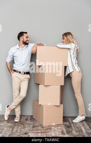 Photo of nice european couple in casual clothing looking at each other with cardboard boxes isolated over gray background Stock Photo