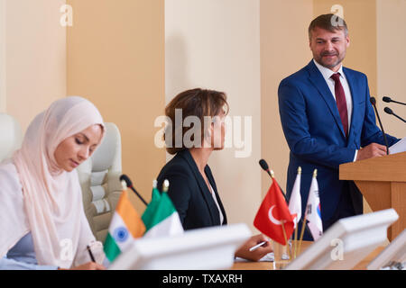 Young confident speaker in elegant suit standing by tribune Stock Photo