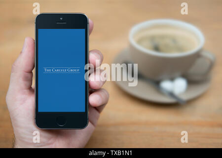 A man looks at his iPhone which displays the Carlyle Group logo (Editorial use only). Stock Photo