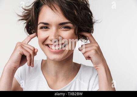 Portrait of caucasian woman with short brown hair in basic t-shirt plugging her ears with fingers isolated over white background Stock Photo