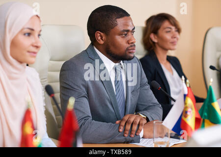 Serious young African-american speaker listening to one of foreign colleagues Stock Photo