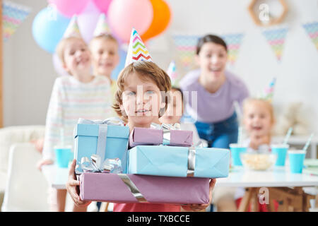 Adorable little boy in birthday cap holding pile of birthday presents Stock Photo
