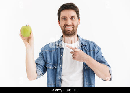 Portrait of a handsome bearded man wearing casual clothes standing isolated over white background, showing green apple, pointing Stock Photo