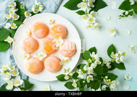 Multi-colored Japanese ice cream Mochi in rice dough and Jasmine flowers on a concrete blue background. Traditional Japanese dessert on a white plate. Stock Photo