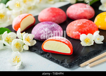 Multi-colored Japanese ice cream Mochi in rice dough and Jasmine flowers on a concrete blue background. Traditional Japanese dessert on a black slate. Stock Photo