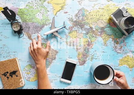 Top view of young woman planning her vacation using world map while drinking coffee - Tourist pointing the next travel destination Stock Photo