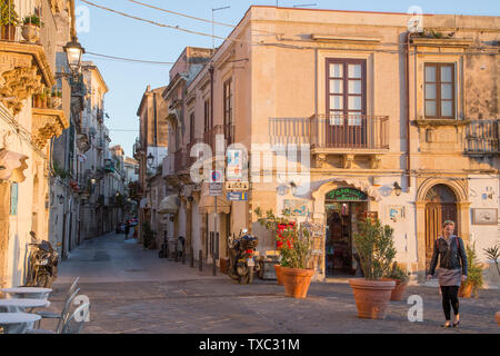 Syracuse, Italy - March 12, 2018: the beautiful streets of Ortigia, Syracuse, with golden sunset light on its buildings and people Stock Photo