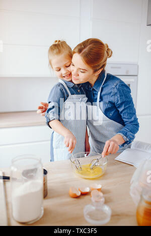 https://l450v.alamy.com/450v/txc3f5/a-young-and-beautiful-mother-in-a-blue-shirt-and-apron-is-preparing-dinner-at-home-in-the-kitchen-along-with-her-little-cute-daughters-with-light-hai-txc3f5.jpg