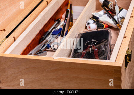 A wooden toolbox full of an artit's tools.  Clearly visible are a compass, a mechanical pencil, artist's brushes and acrylic paint tubes. Stock Photo