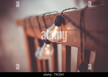 Close up shot of lit light bulbs with black wires hanging on a wooden vertical surface Stock Photo