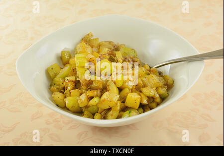 Yellow summer squash and zucchini with onion side dish in white serving bowl with serving spoon on tablecloth Stock Photo