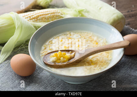 Corn egg soup corn soup in a ceramic bowl with a wooden spoon with a background of gray cloth, eggs and corn. Stock Photo