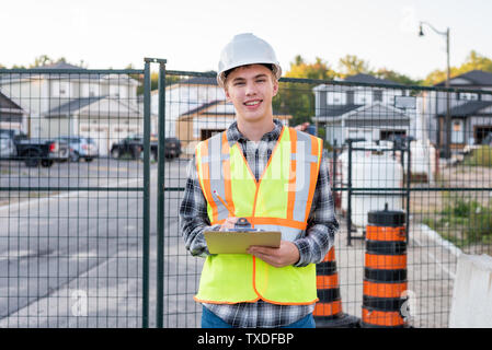 Happy young construction worker wearing safety gear and holding a clipboard. Stock Photo
