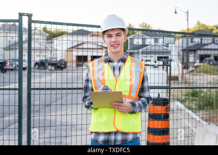 Happy young construction worker wearing safety gear and holding a clipboard. Stock Photo