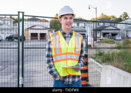 Happy young construction worker wearing safety gear and holding a clipboard. Stock Photo