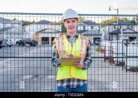 Happy young construction worker wearing safety gear and holding a clipboard. Stock Photo