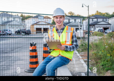 Happy young construction worker wearing safety gear and holding a clipboard. Stock Photo