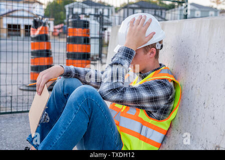 Upset and frustrated construction worker sitting down at a job site. Stock Photo