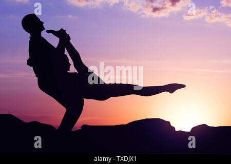 Silhouette of couple practicing yoga against sun. Acro yoga at sunrise concept Stock Photo