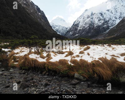 A fresh stream flows through a valley between white-capped mountains Stock Photo