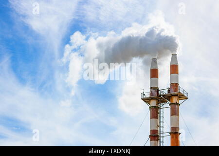 Close up image of two smoke stacks billowing smoke into the atmosphere against blue sky with copy space Stock Photo