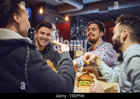 Happy friends eat burgers, drink beer in a bar. People in a fast food restaurant. Stock Photo