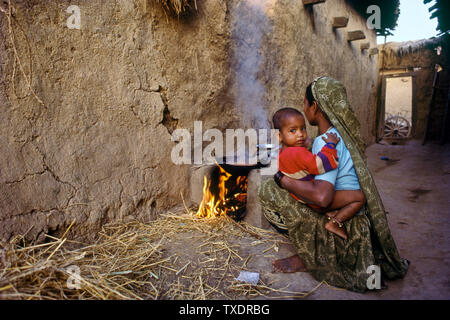 Woman with child in lap cooking on traditional stove, Gujarat, India, Asia Stock Photo