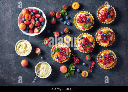 Beautiful delicious summer tartlets with fresh custard creamy filling topped with raspberries, apricots, blueberry, strawberry, red currants on a conc Stock Photo