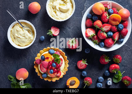 Beautiful delicious summer tart with fresh custard creamy filling topped with raspberries, apricots, blueberry, strawberry, red currants on a concrete Stock Photo