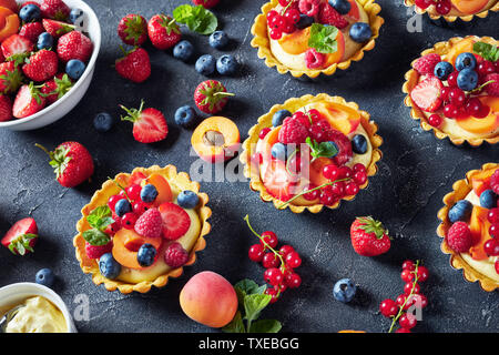 close-up of summer tartlets with lemon custard creamy filling topped with raspberries, apricots, blueberry, strawberry, red currants and fresh mint on Stock Photo
