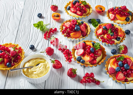 close-up of french desserts - tarts with lemon custard cream filling topped with raspberries, apricots, blueberry, strawberry, red currants and fresh Stock Photo