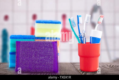 Red container with toothbrushes and toothpaste on a wooden surface and washcloths in the background of the bathroom Stock Photo