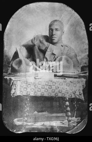 World War I    :  African-American soldier seated behind table, pencil in hand, with two hats on table Stock Photo