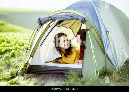 Young lovely couple in bright sweaters enjoying nature, lying in the tent while traveling high in the mountains Stock Photo
