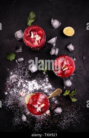 Blended strawberry shake smoothie with whole strawberries, ice and lemon in glasses and ice cubes on black background. Healthy eating diet concept. Stock Photo