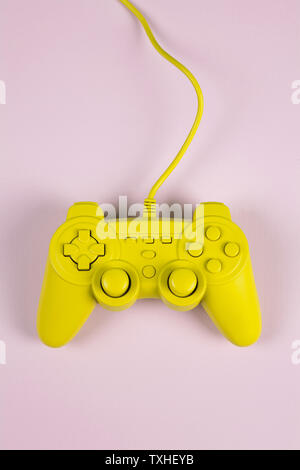 a yellow painted video game controller on a plain pink background. Minimal color still life photography Stock Photo