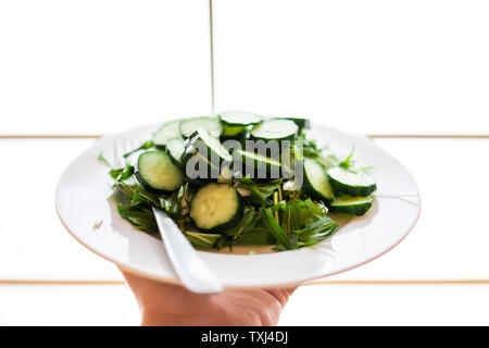 Home or restaurant with hand holding green salad dish closeup with Japanese cucumbers and mizuna greens with background of shoji Stock Photo